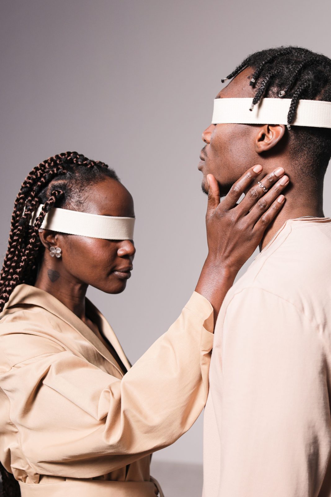 Two people facing each other wearing blindfolds, one hand resting on the other's neck